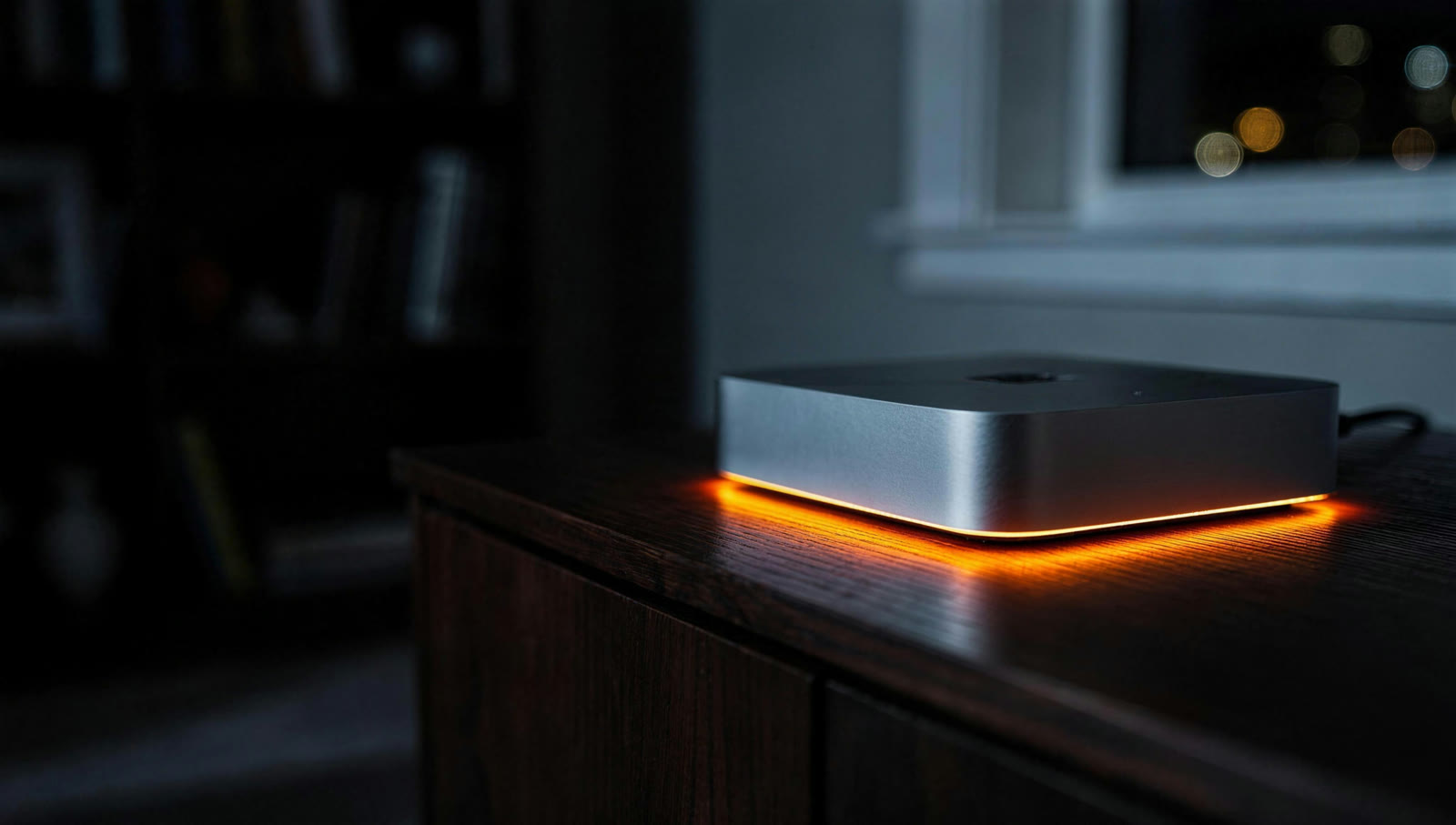 A Mac mini glowing orange on a black desk at night.